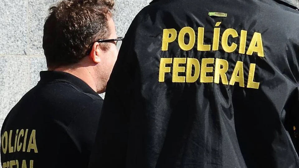 Provas do concurso Polícia Federal: polícias federais de costas. É possível ler "Polícia Federal" no uniforme de um dos policiais